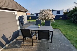 Une terrasse extérieure avec une table et des chaises, une table abritée, une plante en pot et un arbre en fleurs.