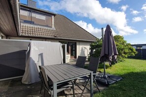 An outdoor patio with a table and chairs, a covered grill, and a patio umbrella. - Holiday apartment with 2 bedrooms (Cuxhaven)