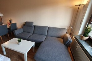 Un salon moderne avec un canapé d’angle gris, une table basse blanche et un lampadaire.