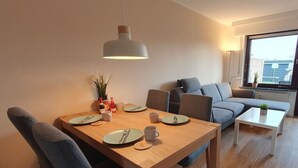 Ein modernes Wohnzimmer mit Esstisch für Zwei, einem grauen Sofa und einem kleinen weißen Couchtisch.