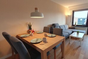 Un salon moderne avec une table à manger pour deux personnes, un canapé gris et une petite table basse blanche.