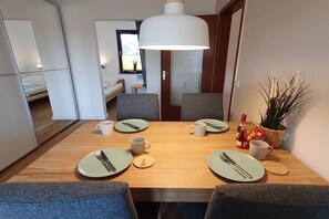 A compact hotel room with a dining table set for two, a bed, a small kitchenette, and a large window. - Holiday apartment with 2 bedrooms (Cuxhaven)