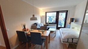 Ein kompakter Wohnbereich mit Essplatz, einer Couch, einem Bett und Blick durch eine Glastür.