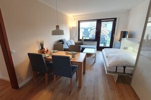 Un espace de vie compact comprenant un coin repas, un canapé, un lit et une vue à travers une porte vitrée.