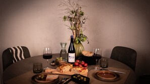 Ein runder Esstisch mit einer Weinflasche, Gläsern, Brot, Oliven, Tomaten und einer Pizza.