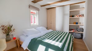 Ein Schlafzimmer mit Bett, Fenster, Kleiderschrank und einem Regal mit Taschen.