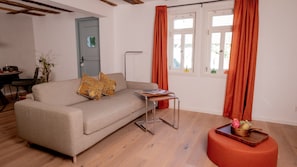Een woonkamer met een bank, een bijzettafeltje, een vloerlamp en een raam met gordijnen.