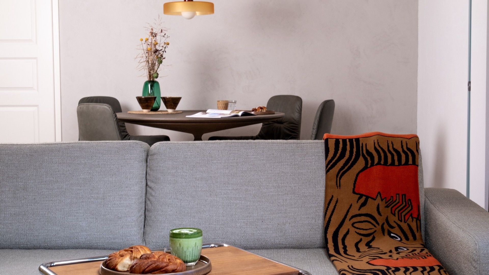 A modern living room with a grey sofa, a wooden side table with a green candle, and a decorative tiger print pillow.