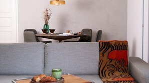 Un salon moderne avec un canapé gris, une table d’appoint en bois sur laquelle est posée une bougie verte, et un coussin décoratif à motif de tigre.