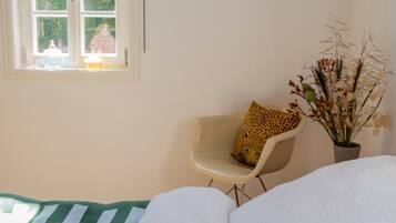 A bedroom with a bed, a chair with a leopard print pillow, a potted plant, and a window with a view of a brick building.