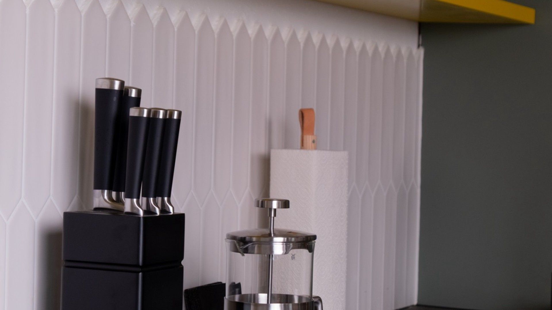 Une cuisine au design moderne, avec un appareil électroménager noir, une machine à café en acier inoxydable et un couteau à manche en bois, le tout sur un mur blanc.