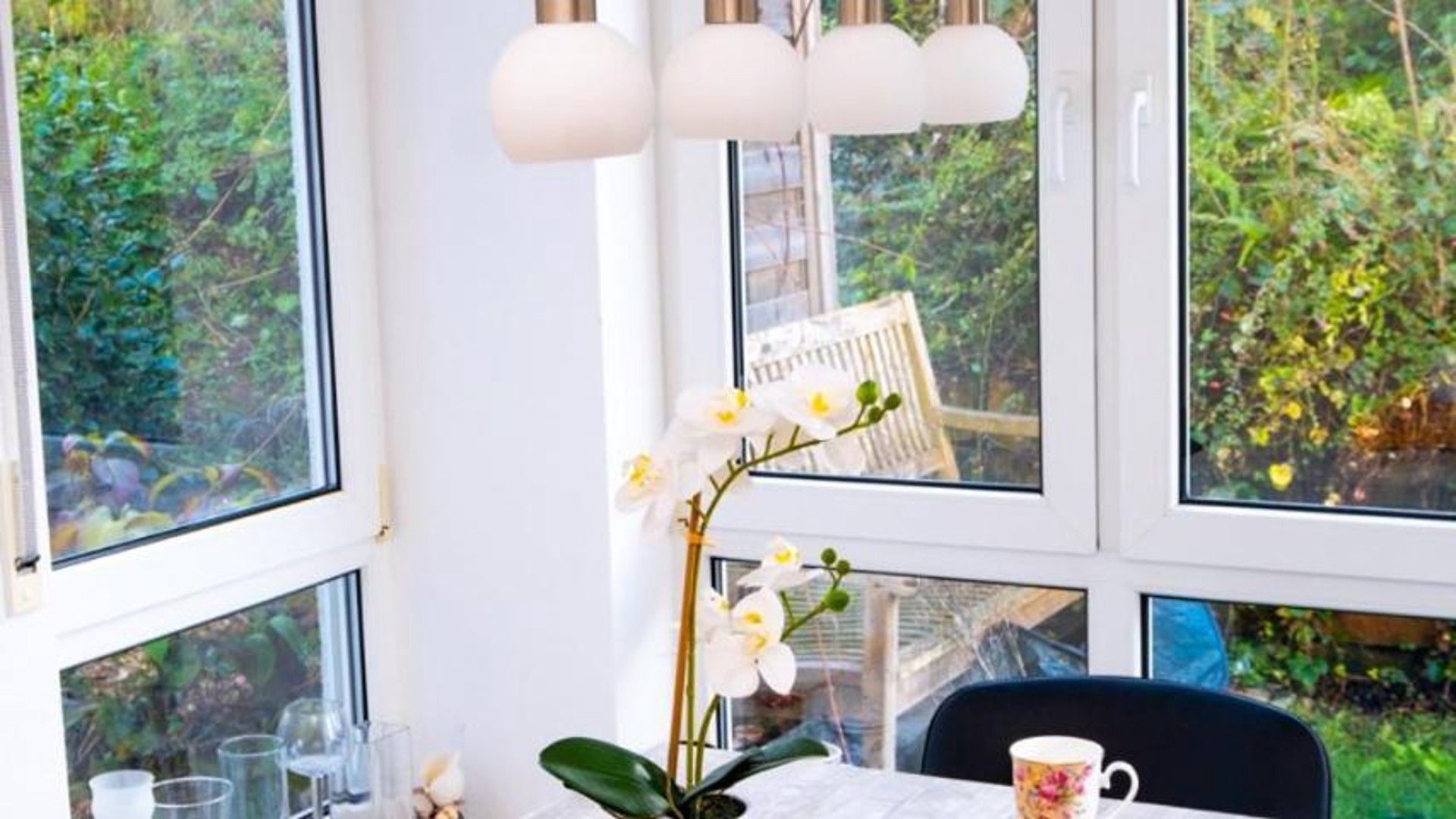 A room with large windows, a table with a plant, and a chair.