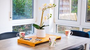 Una mesa de comedor con una bandeja, dos tazas, una planta y una ventana con vista a follaje.