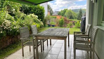 Eine Terrasse im Freien mit einem Holztisch und vier Stühlen, umgeben von üppiger Vegetation und einer Steinmauer.