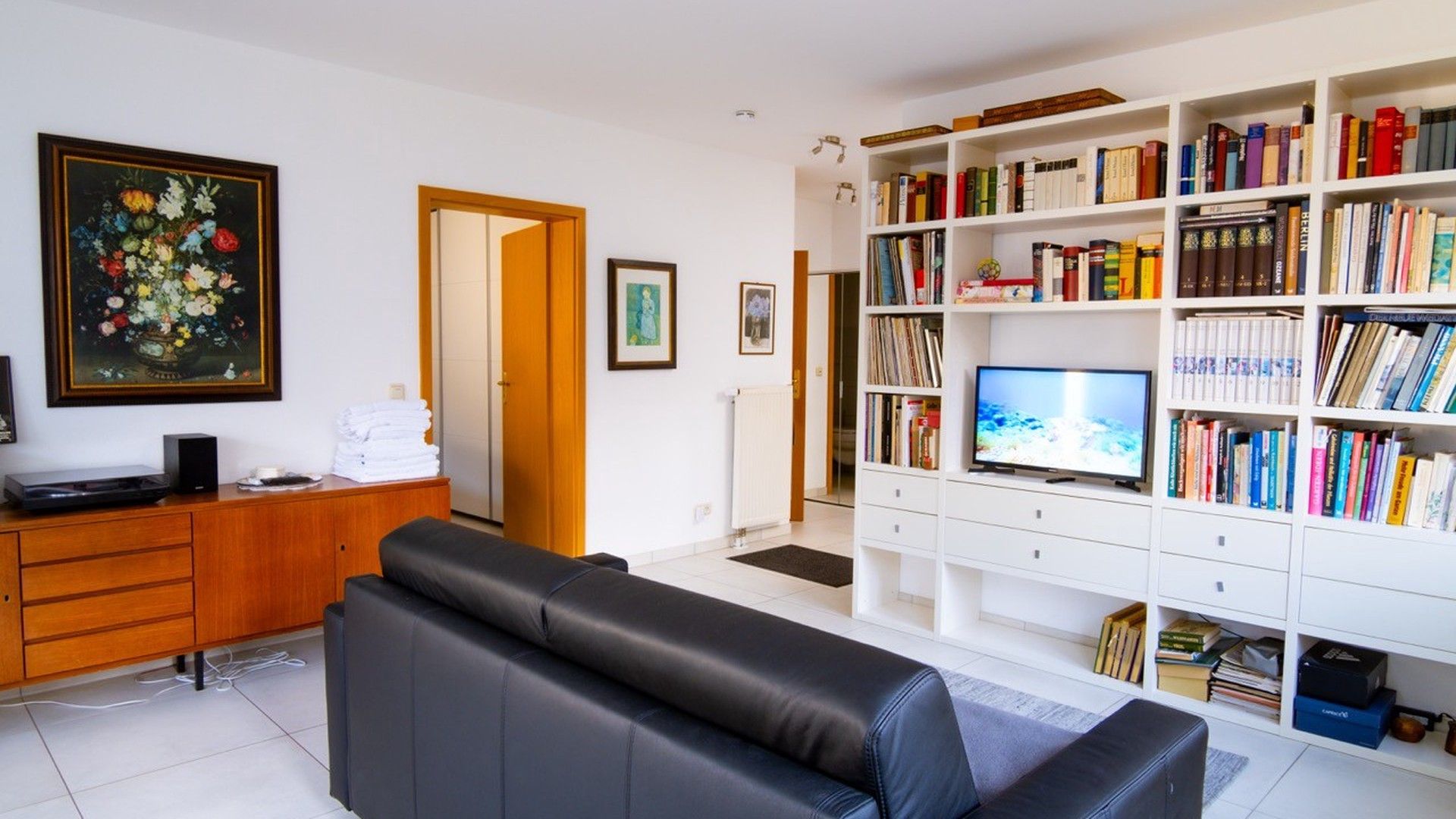 A living room with a sofa, a television, a bookshelf, and a painting.