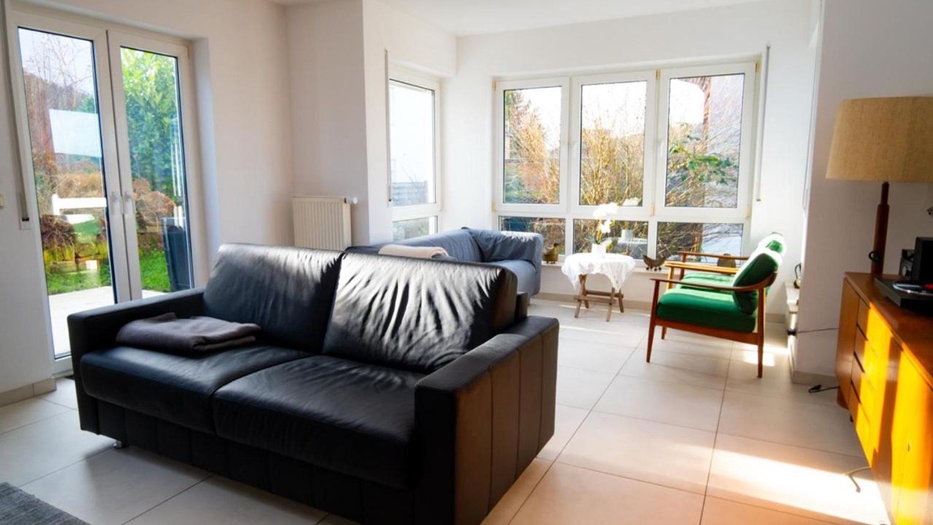 A modern living room with a black sofa, a green chair, and a dining table with chairs.