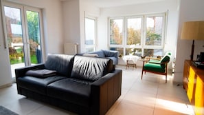 Un salon moderne avec un canapé noir, un fauteuil vert et une table à manger avec des chaises.