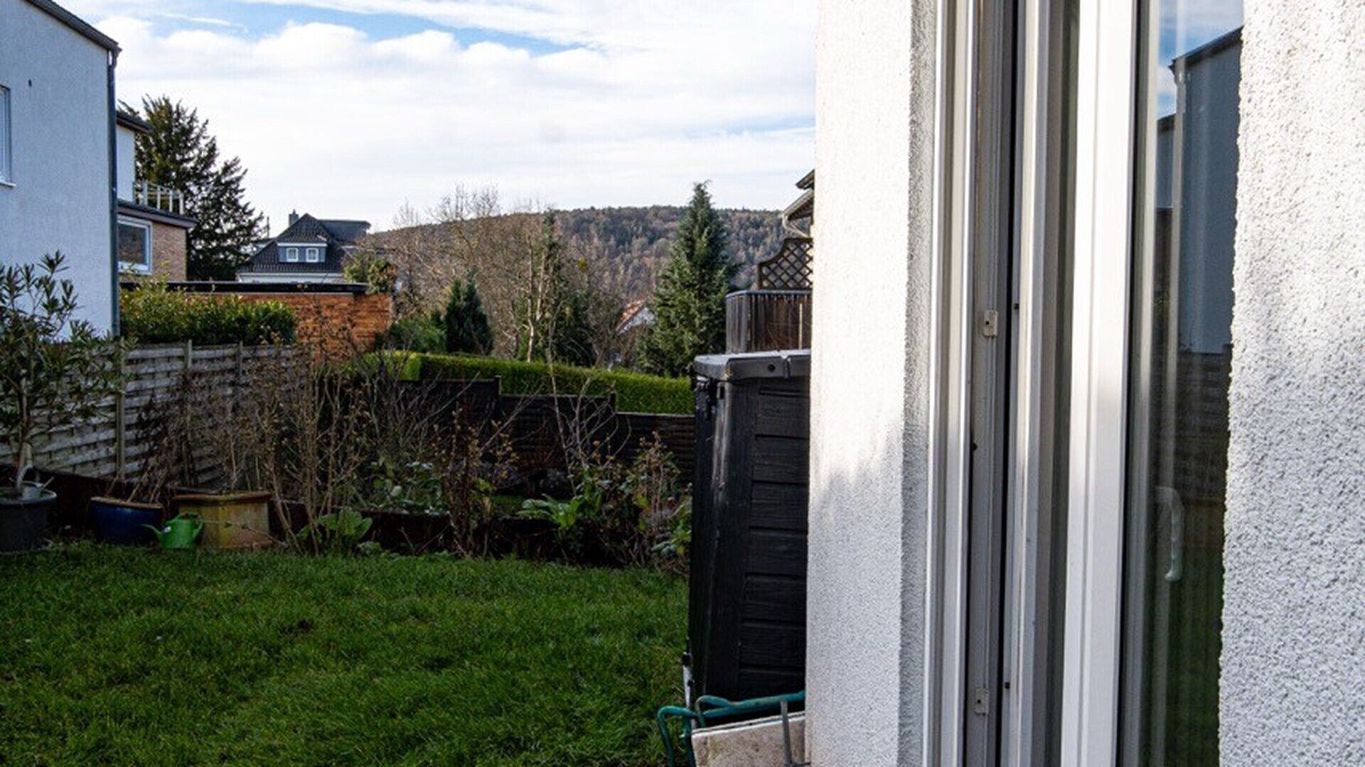 A residential property with a well-maintained lawn, a wooden fence, and a view of a hill.