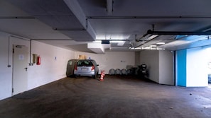 Eine Parkgarage mit einem Auto in der Mitte, einer blauen Tür rechts und einem Feuerlöscher an der Wand.