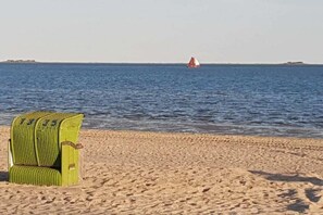 Une plage avec une chaise verte et un voilier à l’horizon.