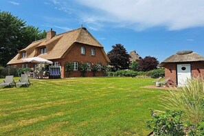 Une maison traditionnelle en briques, avec un toit de chaume, une pelouse bien entretenue et un espace salon extérieur.