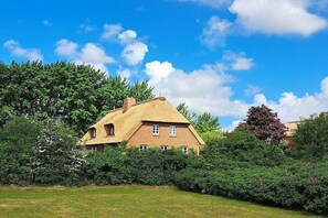 Une maison au toit de chaume, entourée d’une végétation luxuriante et sous un ciel bleu azur.