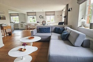 Un salon moderne avec un canapé gris, deux tables basses blanches et un coin repas comprenant une table et des chaises blanches.