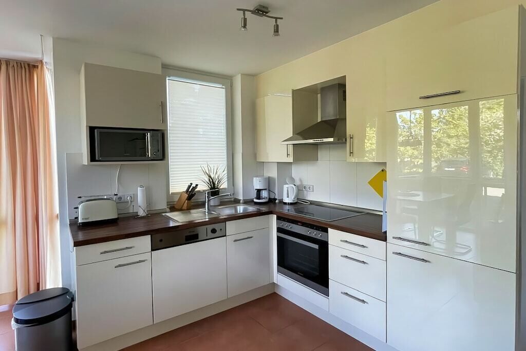 Una cocina moderna con armarios blancos, microondas, cafetera y lavavajillas.