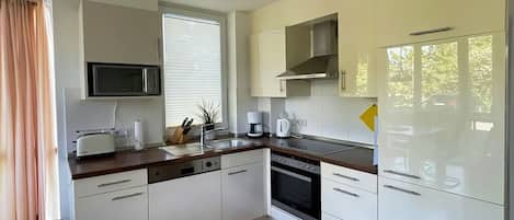 Una cocina moderna con armarios blancos, microondas, cafetera y lavavajillas.