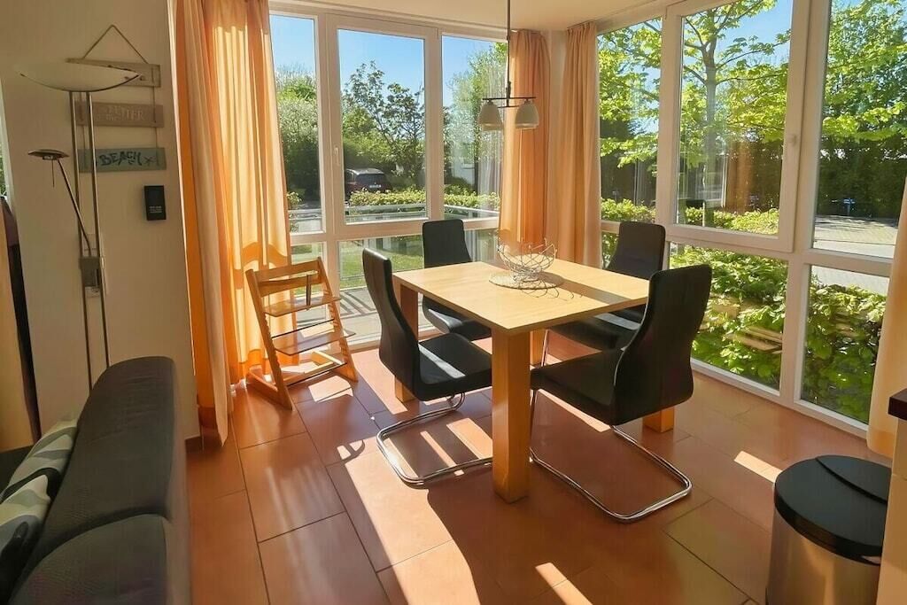 Un comedor con mesa y sillas, ventanas amplias y vistas al exterior con vegetación.