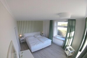 Ein Schlafzimmer mit einem Doppelbett, einem Nachttisch mit Lampe, einem Fenster mit Vorhängen und einer Heizung.