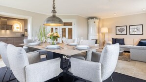 Uma área de refeições com uma mesa posta para seis pessoas, rodeada por seis cadeiras estofadas cinzentas.