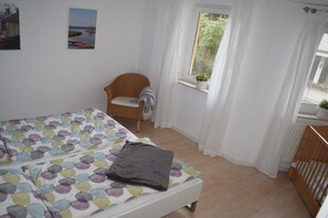 Un dormitorio con cama, una silla, una ventana con cortinas y vistas al exterior.