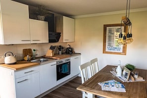 Une cuisine moderne avec des meubles blancs, un plan de travail en bois et une table à manger avec un set de table.