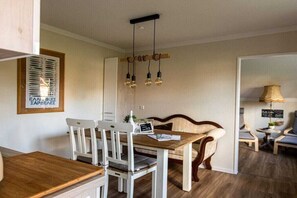 A dining area with a wooden table and white chairs, a hanging light fixture, and a framed picture on the wall. - Holiday apartment with 1 bedroom (Dornum)