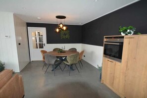 Een eetgedeelte met een ronde tafel en stoelen, een hangende lamp en een keuken met houten kastjes.