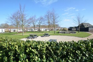 Een woongebied met huizen, een rond grindgebied met picknicktafels, en een haag op de voorgrond.
