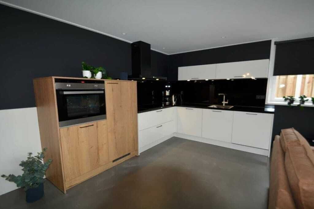 Una cocina moderna con horno empotrado, muebles blancos y encimera negra.