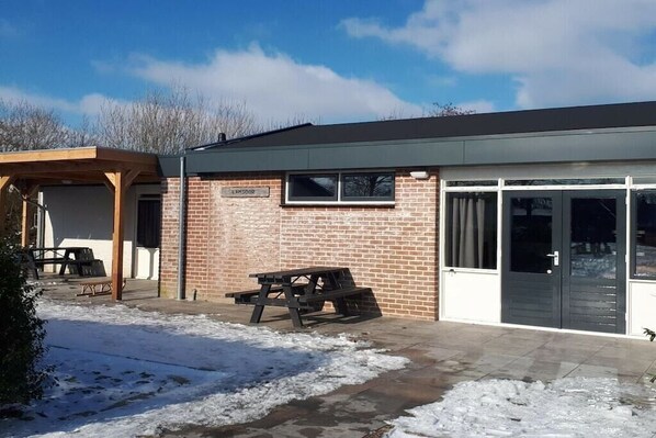 Een bakstenen gebouw met een bord waarop 'LAMSCOOR' staat, een picknicktafel en een overdekt buitenterrein met zitplaatsen.