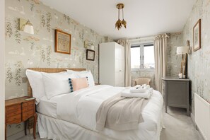 A neatly arranged bedroom with a bed, bedside tables, a wardrobe, and a window with curtains. - New! Delightful 2BR Near Imperial Wharf & Chelsea (Greater London)