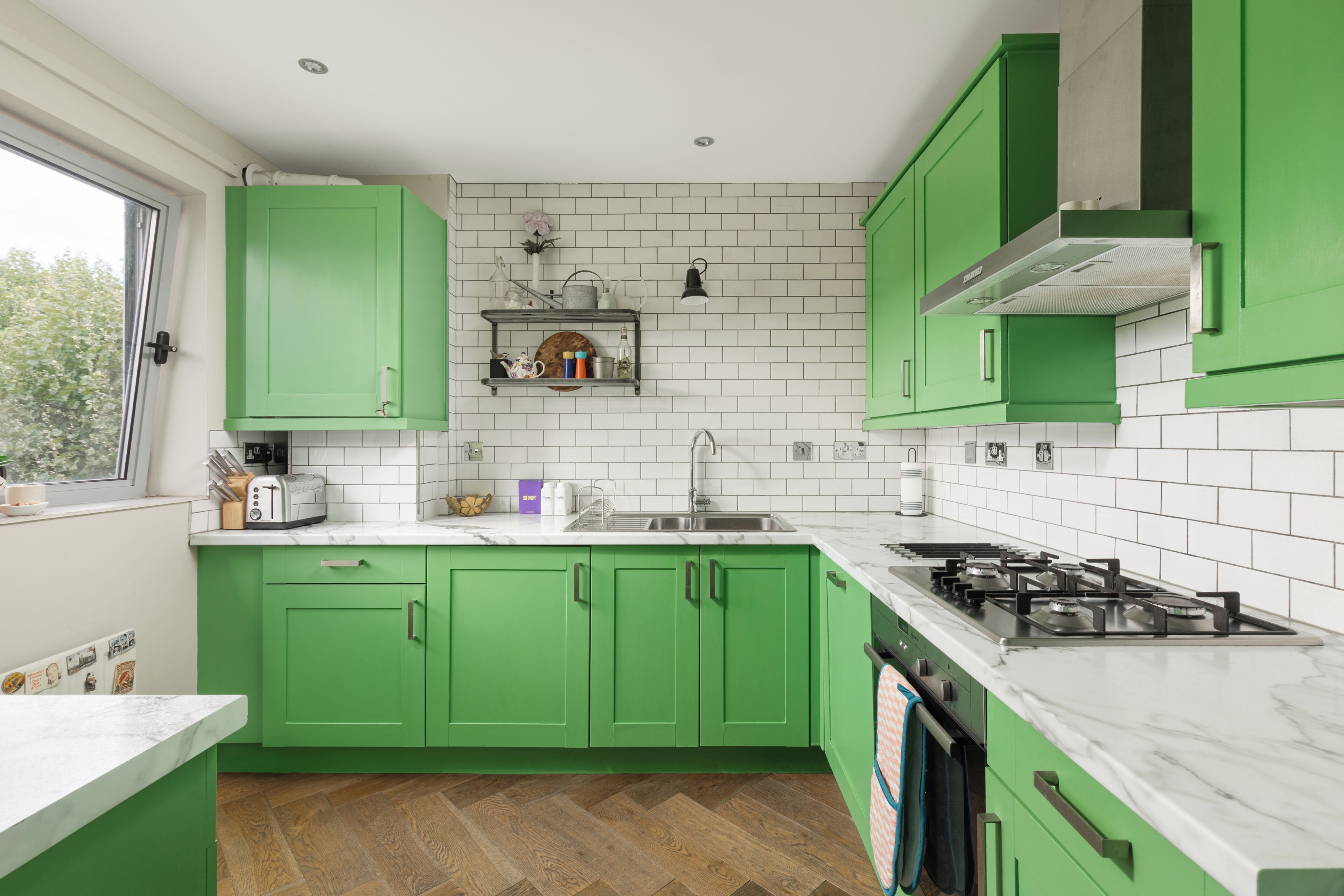 Una cocina con gabinetes verdes, un salpicadero de azulejos blancos y una encimera de mármol.