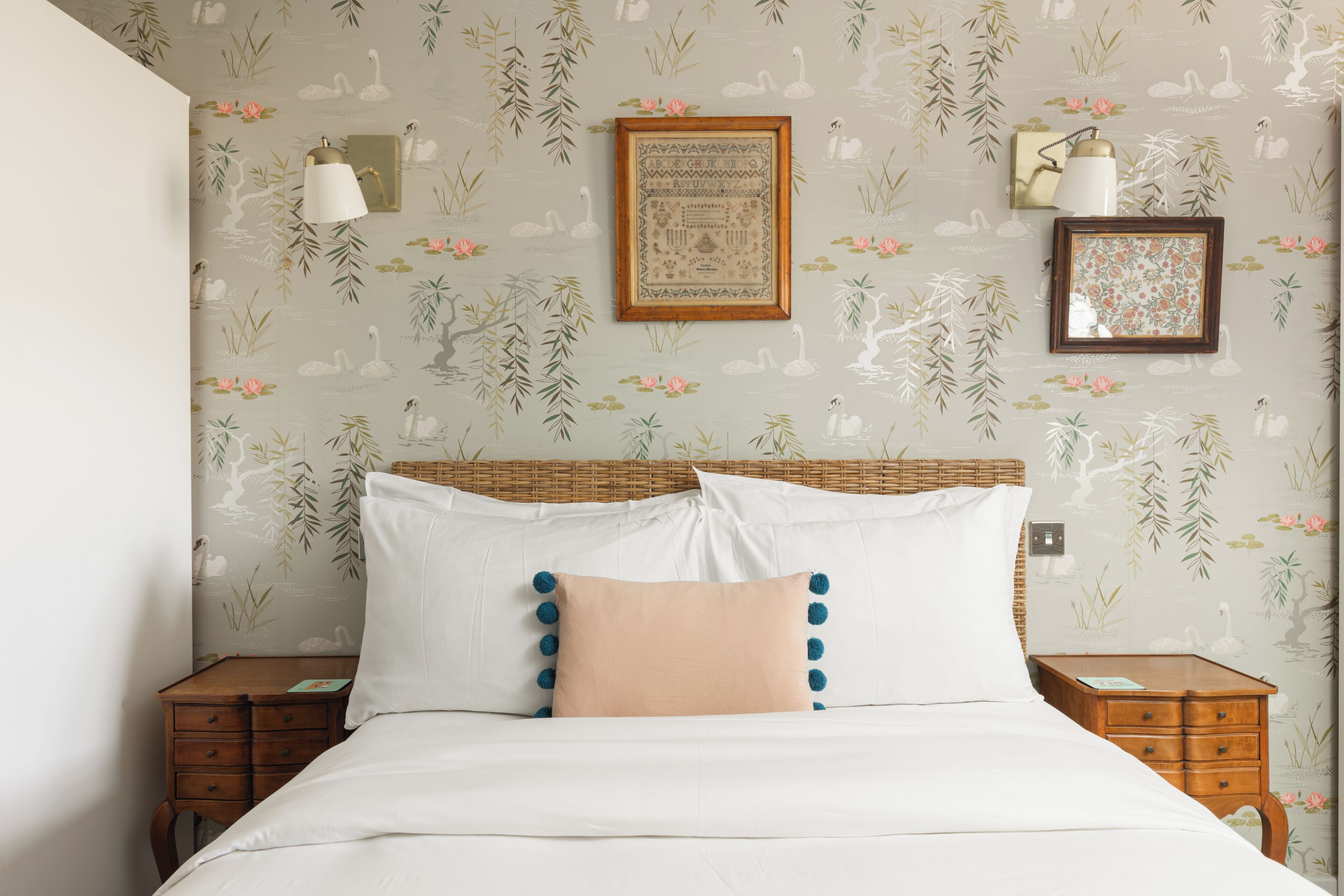 A bedroom with a bed, two nightstands, a wicker headboard, and floral wallpaper.