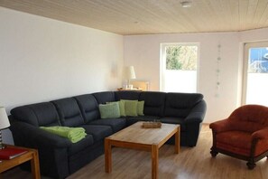 A living room with a dark-colored sofa, a wooden coffee table, and a red armchair. - Holiday home in Fehmarn with swimming pool (Fehmarn)