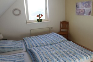 A bedroom with a bed, a chair, a window with a plant, and a wall with a picture. - Holiday home in Fehmarn with swimming pool (Fehmarn)