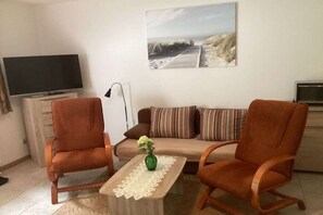 Een woonkamer met een bank, twee fauteuils, een salontafel, een flatscreen televisie en een schilderij aan de muur.