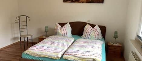 Un dormitorio con una cama, dos mesitas de noche, una silla, una escalera y un cuadro en la pared.