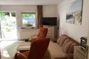 A living room with a sofa, a television, a chair, and a window with a view of the outdoors. - Holiday apartment with 1 bedroom (Seebad Heringsdorf)