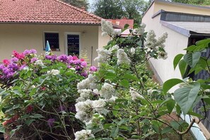 Ein Garten mit blühenden Sträuchern und einem Haus mit einem roten Ziegeldach.
