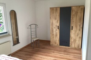 Een kamer met een houten vloer, een kast met een donkere deur, een stoel en een spiegel aan de muur.