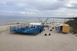 Ein Strand mit einer blauen Konstruktion, vermutlich einer Rettungswache, und einem gelben Gebäude, wahrscheinlich einem Rettungsschwimmerstand.